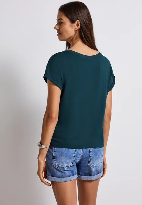 Frau mit dunkelgrünem Shirt und Jeansshorts, steht mit dem Rücken zur Kamera.